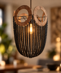A bohemian-style pendant light fixture featuring a black beaded basket body, two circular woven wood sunburst rings, and a glowing warm bulb in the center, shown hanging in a softly blurred indoor setting.