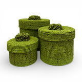 Set of three handcrafted cylindrical storage baskets with olive green wooden beads, matching fitted lids, and decorative beaded handles, perfect for stylish storage and adding vibrant natural texture to living rooms, bedrooms, or bathrooms.