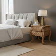 Neatly made bed with a wooden nightstand and lamp in a bedroom setting.