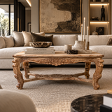An ornate carved wooden coffee table in a styled living room setting, decorated with books, a bowl, and candles, positioned in front of a cream-colored sofa.