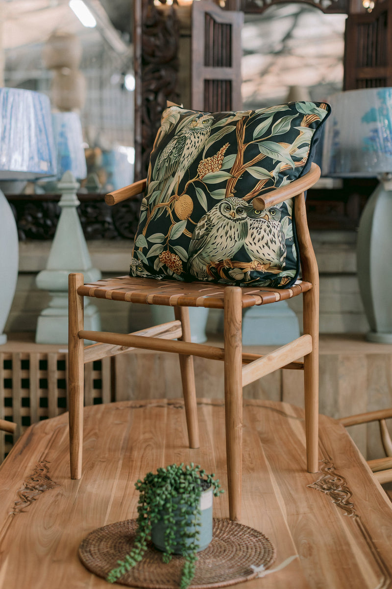Modern solid wood dining chair featuring a natural timber frame, woven leather seat, curved armrests, and a luxury owl and botanical print scatter cushion. A stylish chair that blends Scandinavian design with contemporary and nature-inspired interiors.