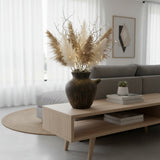 Rustic brown ceramic decorative vase with a textured handcrafted finish and sculptural side spout, styled with pampas grass, natural branches, and warm fairy lights on a modern coffee table, adding organic warmth and timeless elegance to contemporary living spaces.