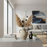 Rustic ceramic amphora vase with a textured stone finish and twin loop handles, styled with pampas grass, decorative branches, and natural botanicals on a modern coffee table, adding timeless organic elegance to contemporary interiors.