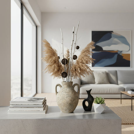 Rustic ceramic amphora vase with a textured stone finish and twin loop handles, styled with pampas grass, decorative branches, and natural botanicals on a modern coffee table, adding timeless organic elegance to contemporary interiors.