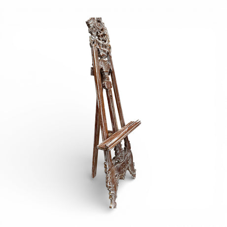 Decorative carved wooden display easel with a distressed whitewashed finish, featuring intricate vintage detailing and an adjustable support, ideal for displaying artwork, wedding signs, mirrors, menus, or decorative pieces.