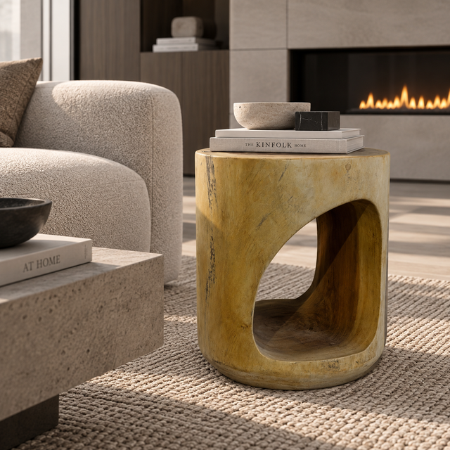 A round wooden side table with a unique hollowed-out cutout in the center, styled in a modern living room next to a beige sofa and in front of a fireplace.