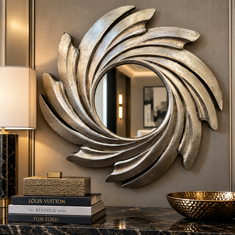 A large decorative wall mirror with a sculptural, swirling shell-like frame in a distressed silver finish, mounted on a textured taupe wall above a marble console table with books and a bowl.