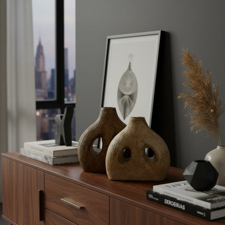 Set of two handcrafted sculptural stoneware vases in warm earthy finishes, featuring unique organic silhouettes with decorative cut-out openings. Perfect for styling consoles, shelves, or coffee tables, these contemporary statement vases bring texture, warmth, and artistic character to modern interiors.