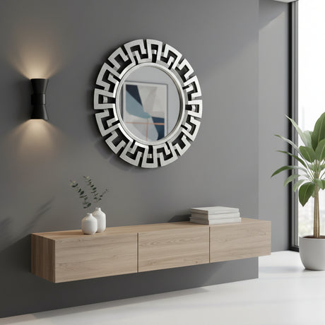 Round silver geometric wall mirror with a bold Greek key-inspired frame, displayed above a floating oak console in a modern living space with minimalist décor.