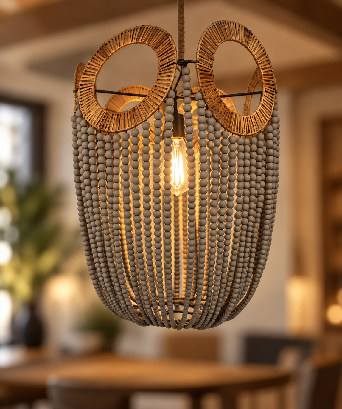 A hanging pendant light fixture with a woven circular top, a central exposed bulb, and many dangling gray beads forming a basket-like shade, shown in a softly blurred indoor room.