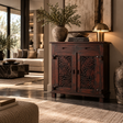 A dark reddish-brown wooden sideboard cabinet with carved leaf-pattern doors, styled in a modern living room with a vase, books, and a lamp on top.