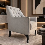 A light gray upholstered accent chair with a tufted backrest and dark wooden legs, shown in a modern living room setting.