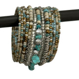Handcrafted multi-layer wrap bracelet featuring turquoise, ivory, silver, and gold-toned seed beads with natural turquoise stone accents, displayed wrapped around a black jewelry display rod.