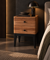 Wooden bedside table with two drawers, round black knobs, a raised tray edge, and tapered black legs.