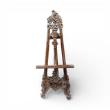 Vintage hand-carved wooden display easel featuring an ornate traditional design with intricate scrollwork and a distressed dark wood finish. Perfect for displaying artwork, framed prints, mirrors, welcome signs, menus, or decorative pieces in homes, galleries, boutique hotels, weddings, and event spaces.