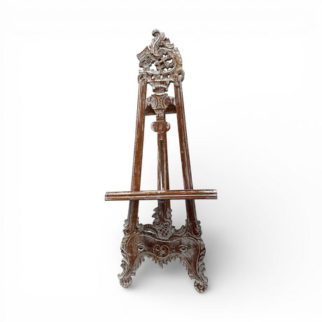 Vintage hand-carved wooden display easel featuring an ornate traditional design with intricate scrollwork and a distressed dark wood finish. Perfect for displaying artwork, framed prints, mirrors, welcome signs, menus, or decorative pieces in homes, galleries, boutique hotels, weddings, and event spaces.