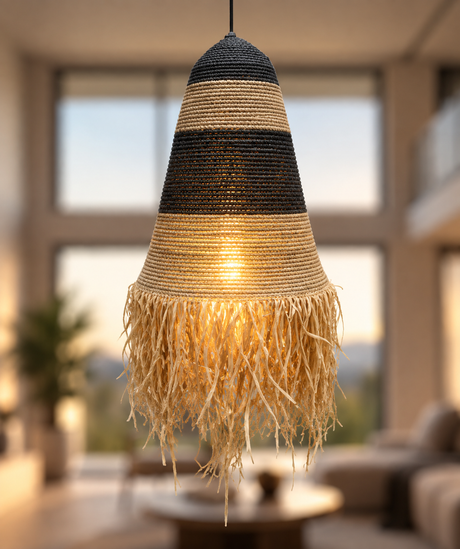 A woven pendant light fixture with black and natural beige horizontal stripes and a long frayed fringe bottom, hanging in a softly blurred modern living room.