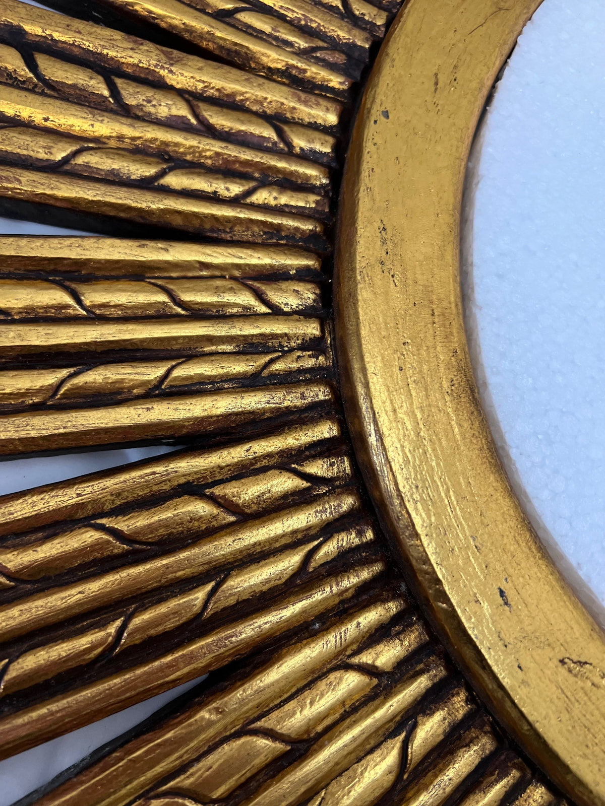 Close-up of an antique gold sunburst wall mirror featuring carved radial detailing, textured accents, and a distressed metallic finish for a luxurious handcrafted look.