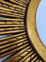Close-up of an antique gold sunburst wall mirror featuring carved radial detailing, textured accents, and a distressed metallic finish for a luxurious handcrafted look.