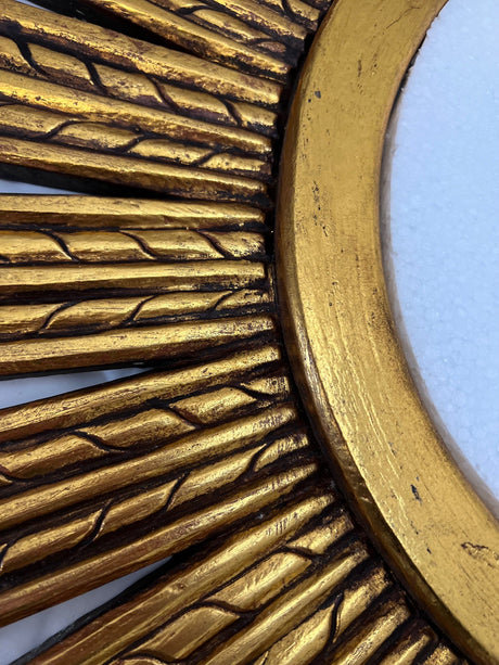 Close-up of an antique gold sunburst wall mirror featuring carved radial detailing, textured accents, and a distressed metallic finish for a luxurious handcrafted look.