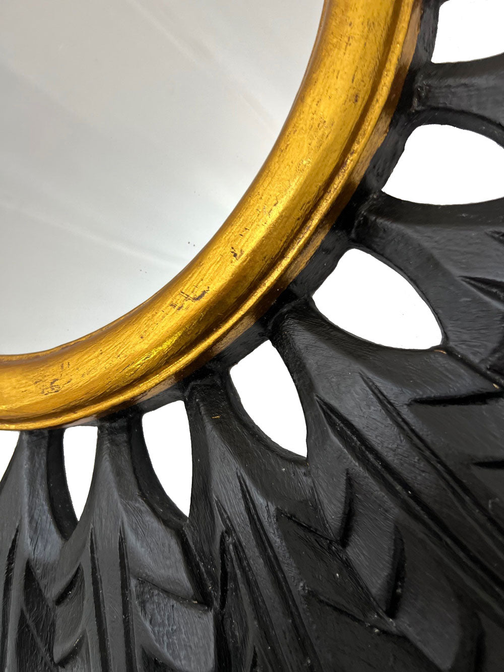 Close-up of a black and gold leaf sunburst wall mirror showcasing its hand-carved leaf detailing, matte black finish, and antique gold inner frame, highlighting the rich texture, artisanal craftsmanship, and striking contemporary elegance.