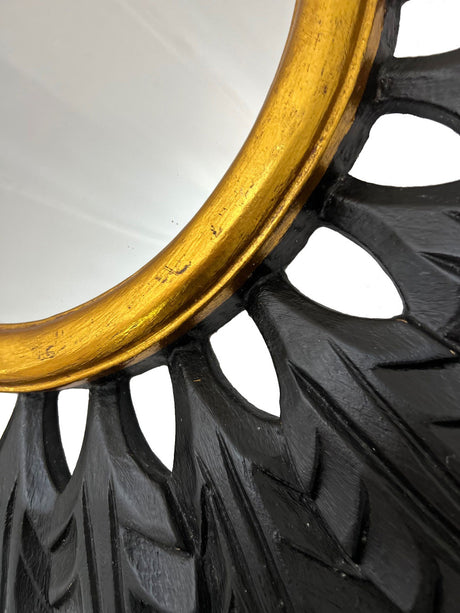 Close-up of a black and gold leaf sunburst wall mirror showcasing its hand-carved leaf detailing, matte black finish, and antique gold inner frame, highlighting the rich texture, artisanal craftsmanship, and striking contemporary elegance.