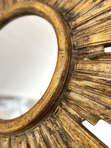 Close-up of a gold sunburst wall mirror featuring a textured radial frame and distressed antique finish, highlighting its handcrafted detail and elegant design.