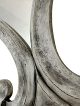 Close-up of an elegant wall mirror featuring a sculptural curved frame with a distressed silver finish, highlighting its handcrafted texture and sophisticated decorative detail.