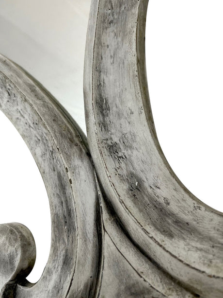 Close-up of an elegant wall mirror featuring a sculptural curved frame with a distressed silver finish, highlighting its handcrafted texture and sophisticated decorative detail.