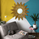 Elegant round gold starburst wall mirror with a textured radiating frame, styled as a striking statement piece in a colourful contemporary living room.