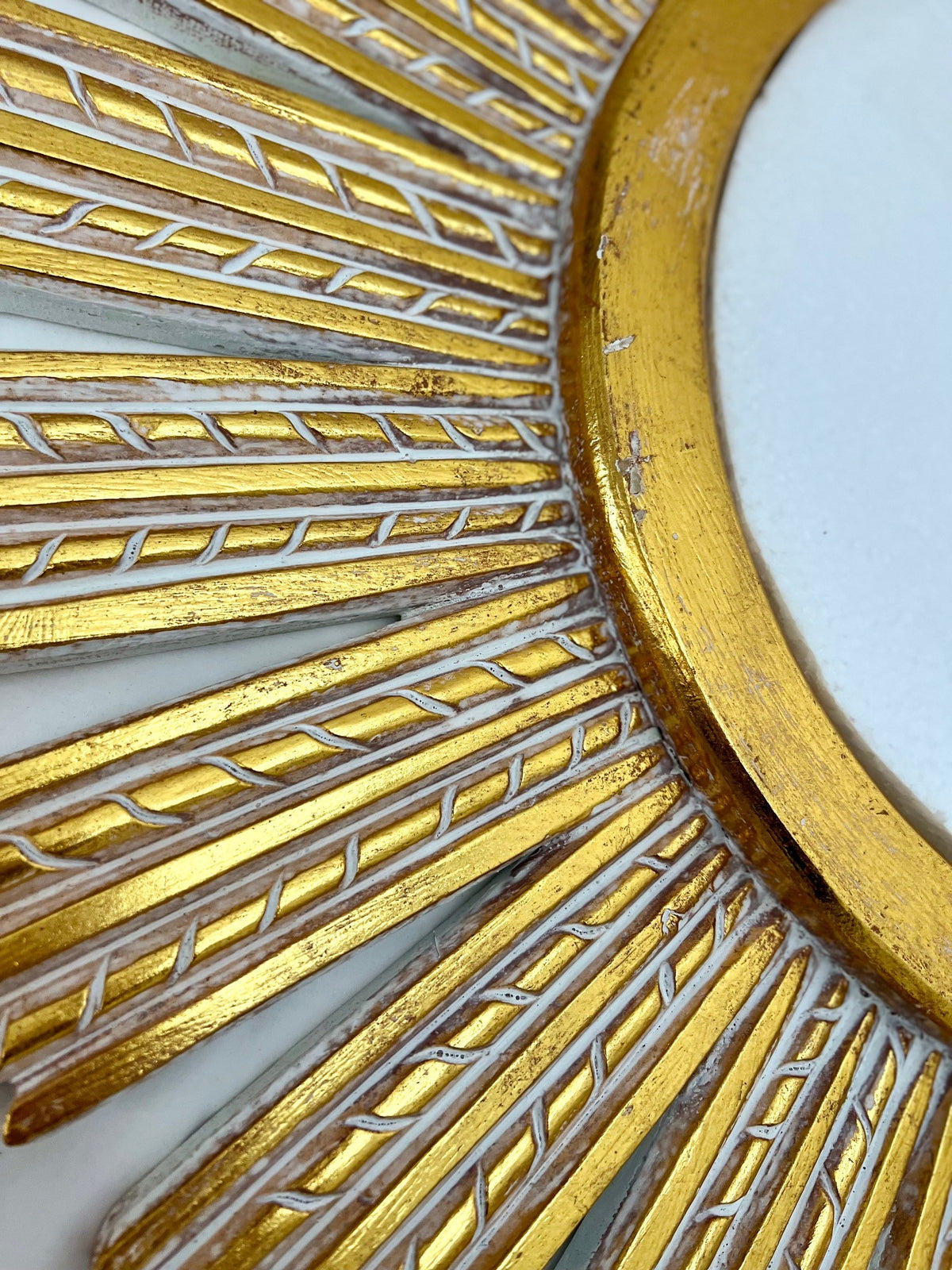 Close-up of an elegant gold sunburst wall mirror featuring a textured radial frame with carved detailing and a distressed metallic finish, highlighting its luxurious handcrafted design.