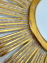 Close-up of an elegant gold sunburst wall mirror featuring a textured radial frame with carved detailing and a distressed metallic finish, highlighting its luxurious handcrafted design.