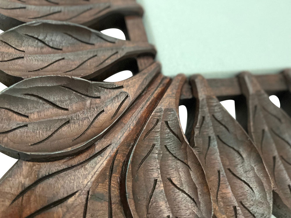 Close-up of a hand-carved wooden leaf wall mirror showcasing its richly grained natural wood finish, intricate leaf detailing, and artisanal craftsmanship, highlighting the warm organic texture and timeless elegance of the decorative frame.