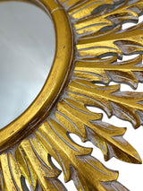 Close-up of an ornate gold wall mirror featuring an intricately carved sunburst leaf frame with a distressed finish, highlighting its handcrafted detail and luxurious design.