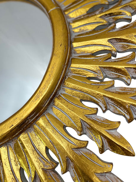Close-up of an ornate gold wall mirror featuring an intricately carved sunburst leaf frame with a distressed finish, highlighting its handcrafted detail and luxurious design.