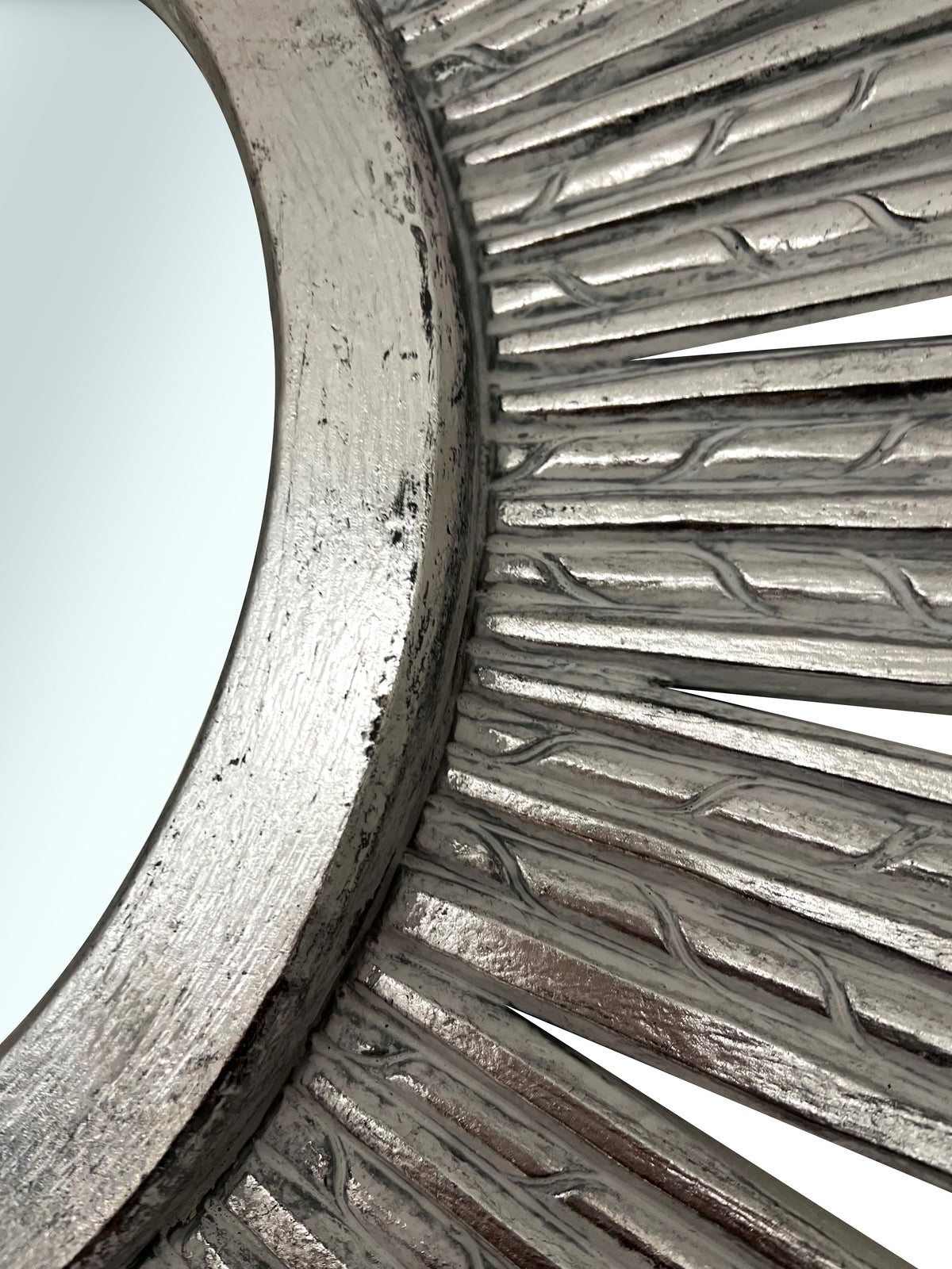 Close-up of an elegant silver sunburst wall mirror featuring a textured radial frame with a distressed metallic finish, highlighting its handcrafted detail and sophisticated design.